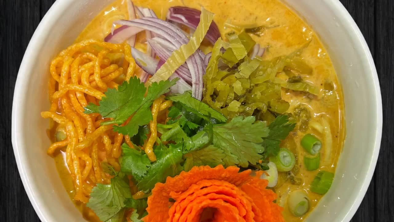 Soup being poured into a bowl of Thai noodles
